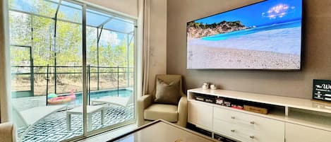 A modern living room with a large TV displaying a beach scene, a glass table, and a sofa.