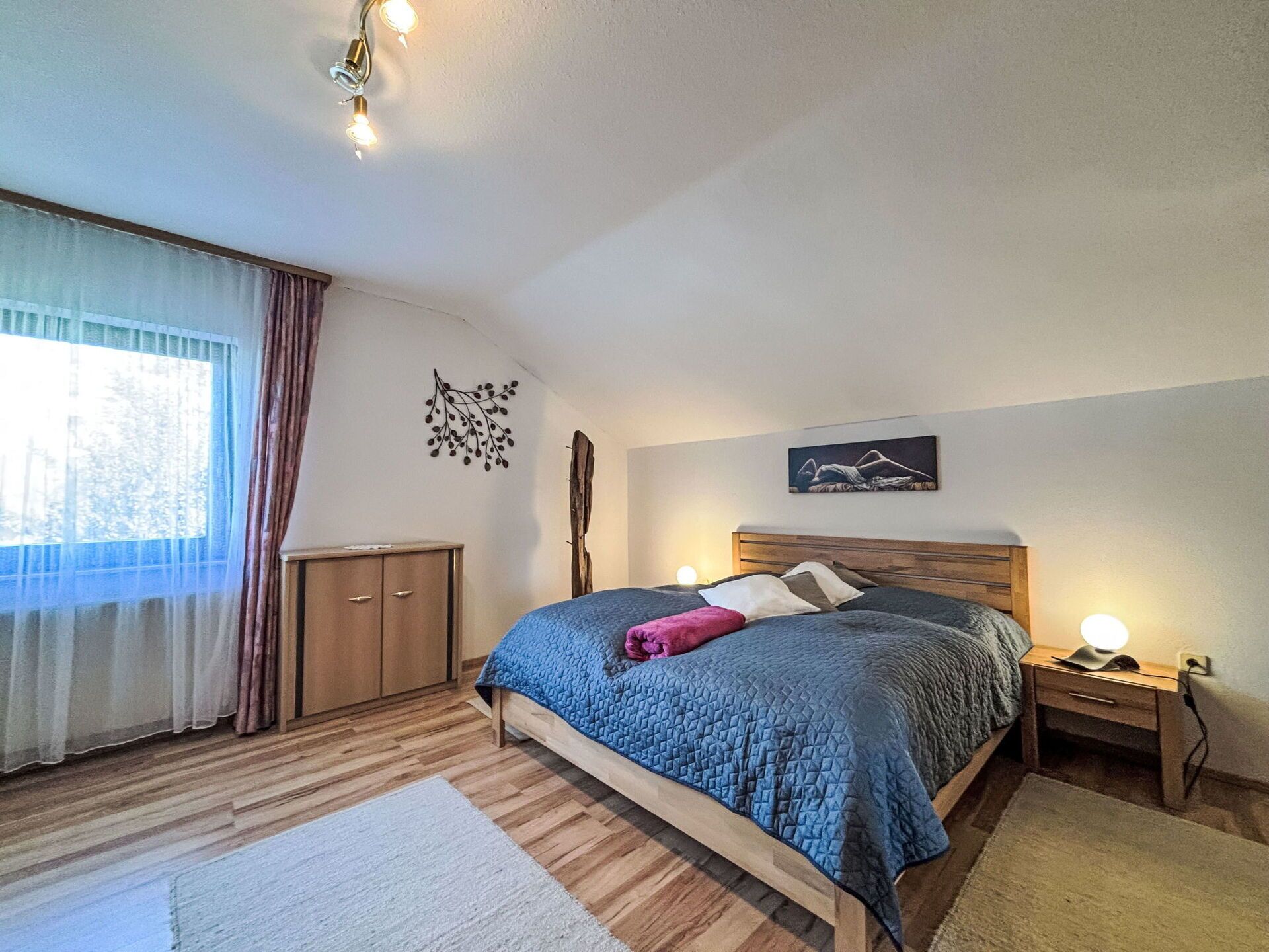 Une chambre à coucher avec un lit en bois, une table de chevet, une armoire et une fenêtre avec des rideaux.