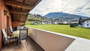Un balcón con vistas a un campo verde y casas, techo de madera y suelo de baldosas.