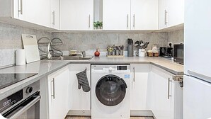 A modern kitchen with white cabinets, a built-in washing machine, and a microwave.