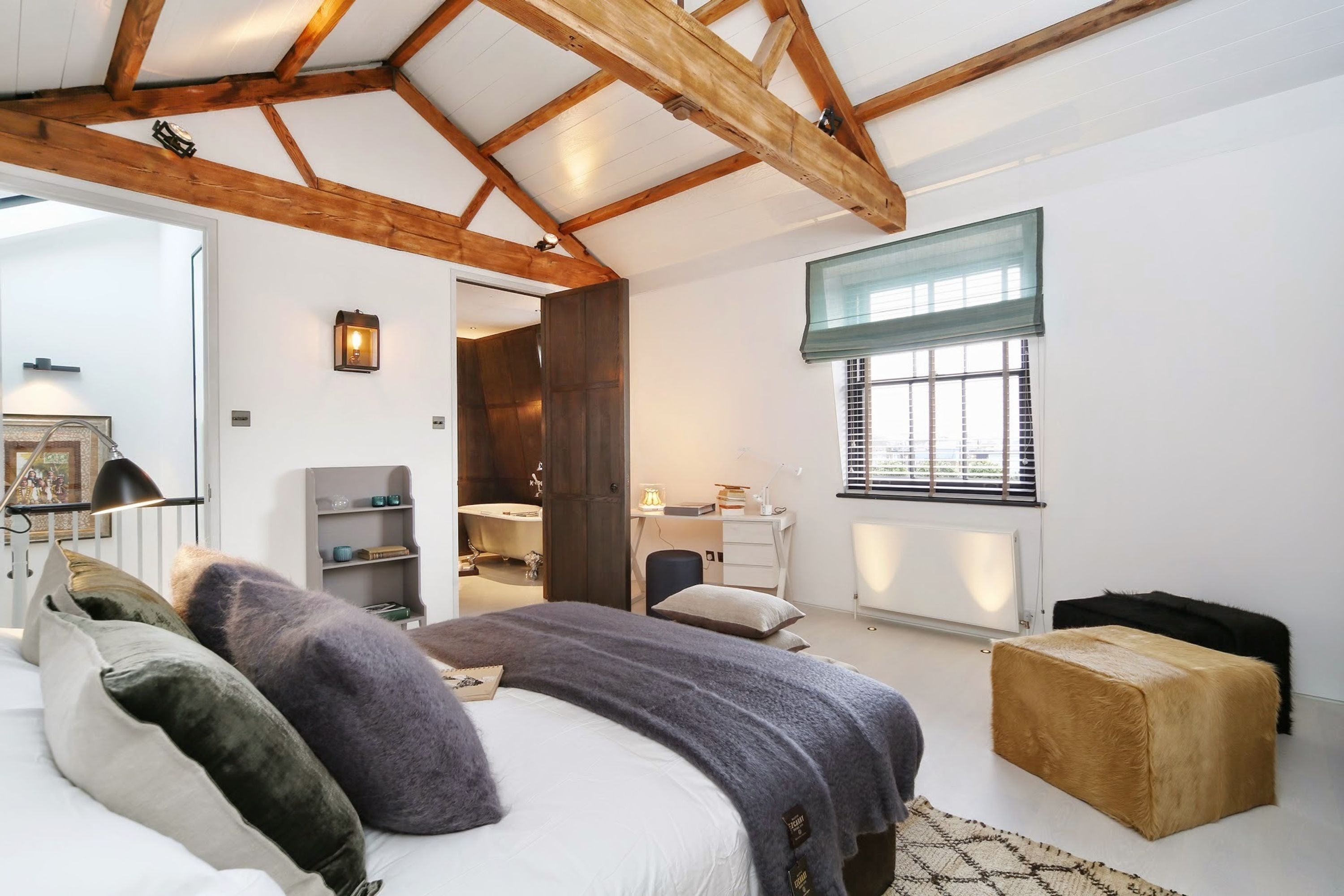 Ein Schlafzimmer mit einem großen Bett, einem Schreibtisch, einem Stuhl, einem Heizkörper und einem Fenster mit Jalousien.