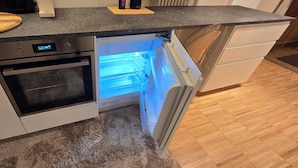 Una cocina con horno integrado, refrigerador con compartimento congelador y tabla de cortar de madera sobre la encimera.