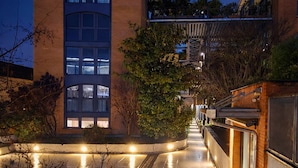Un edificio moderno con fachada de vidrio, una pasarela techada y un camino bien iluminado que conduce a la entrada.