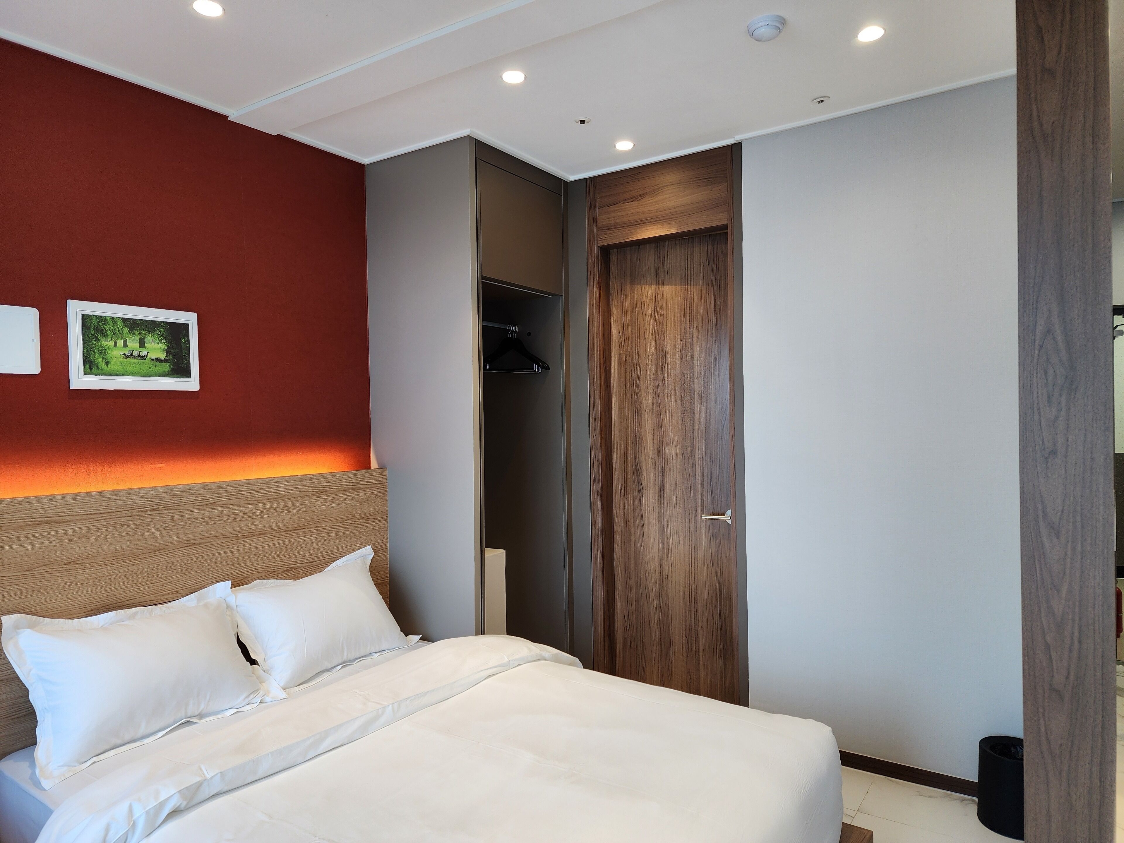 Cama bem arrumada com lençóis brancos, cabeceira de madeira e parede em destaque vermelha.