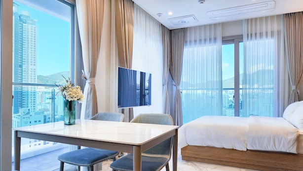 A hotel room with a bed, a TV, a dining table with chairs, and a view of the city. - Parami On (Busan)