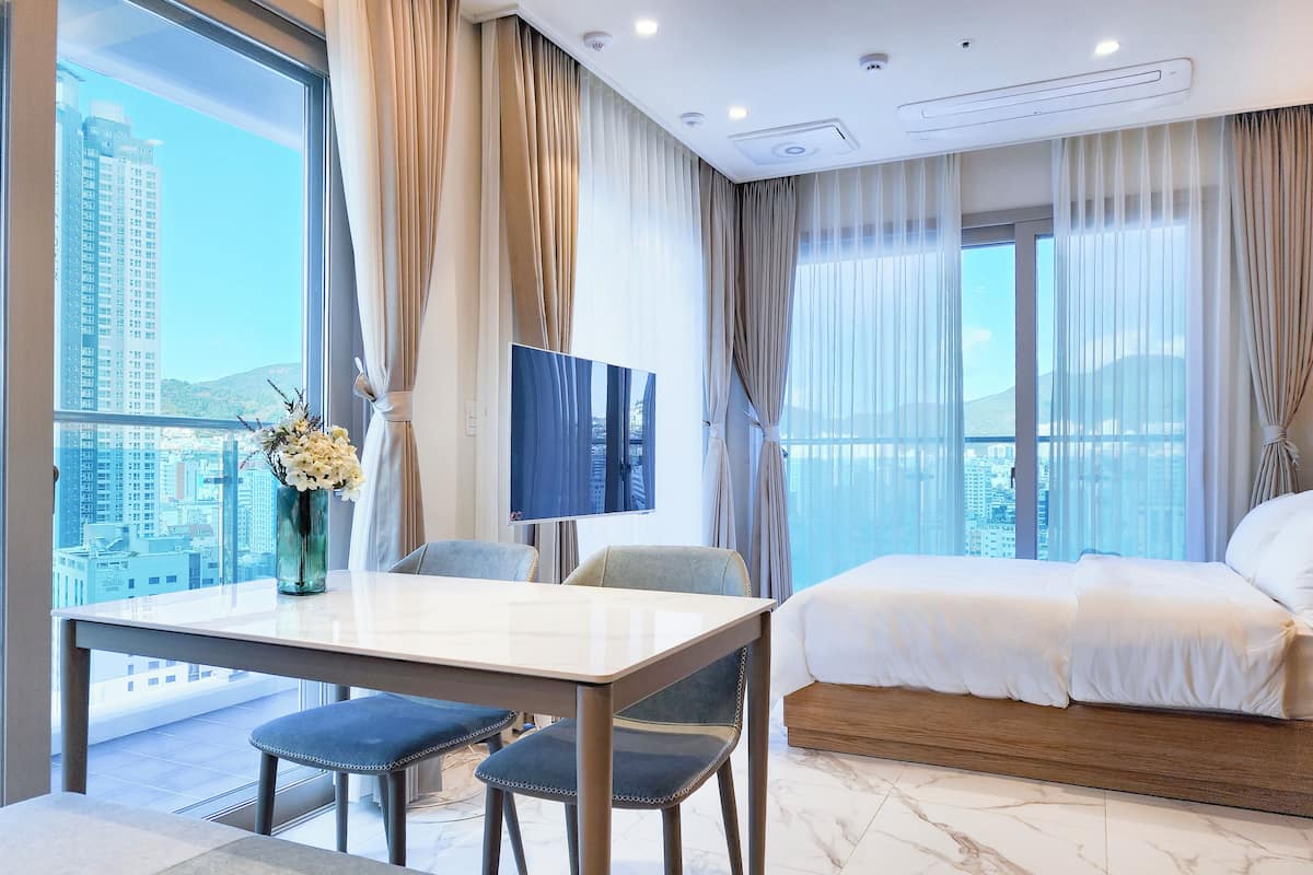 Habitación de hotel con cama, televisión, mesa de comedor y sillas, y vistas a la ciudad.