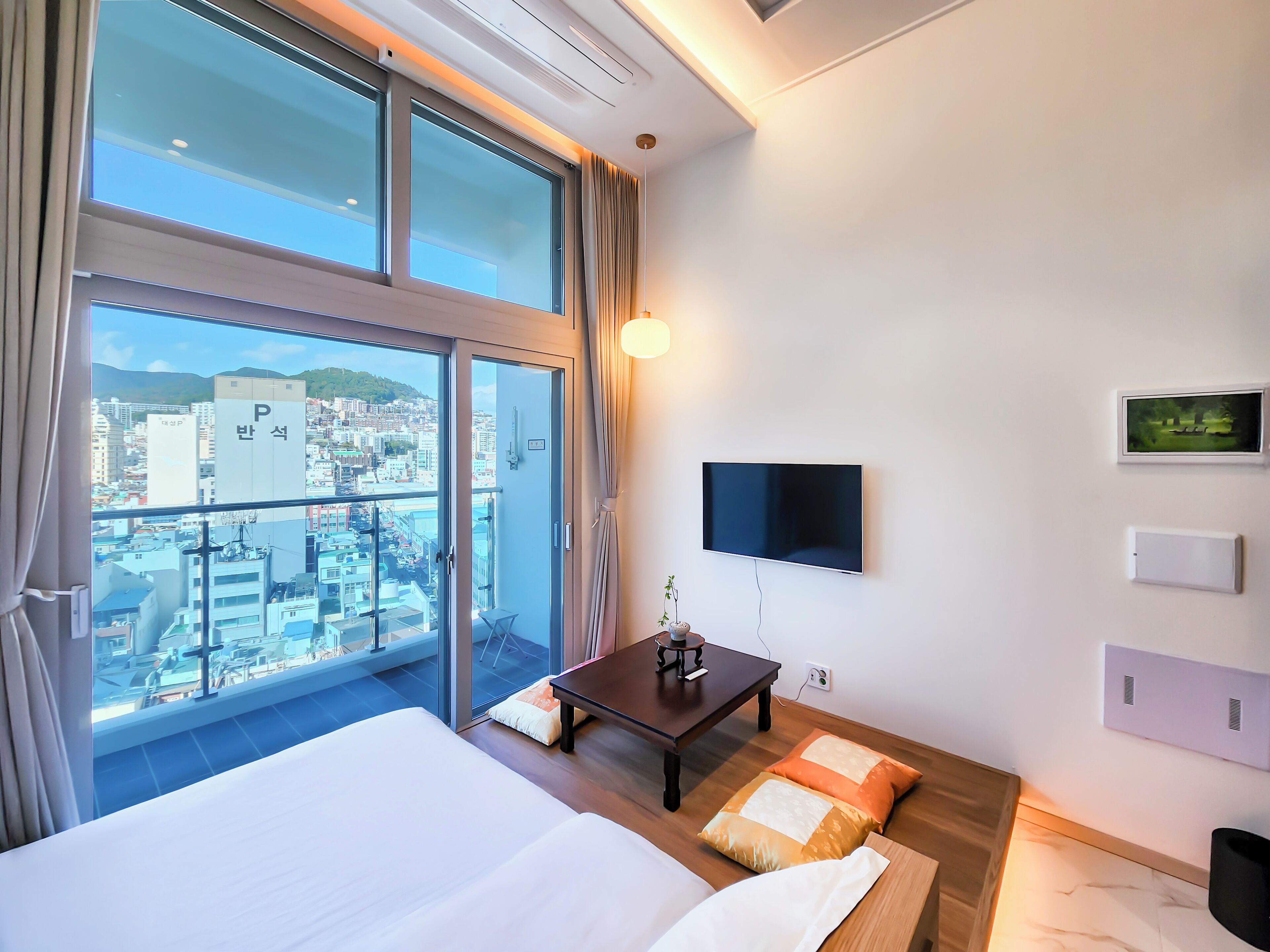A hotel room with a large bed, a small table, a TV, and a city view.