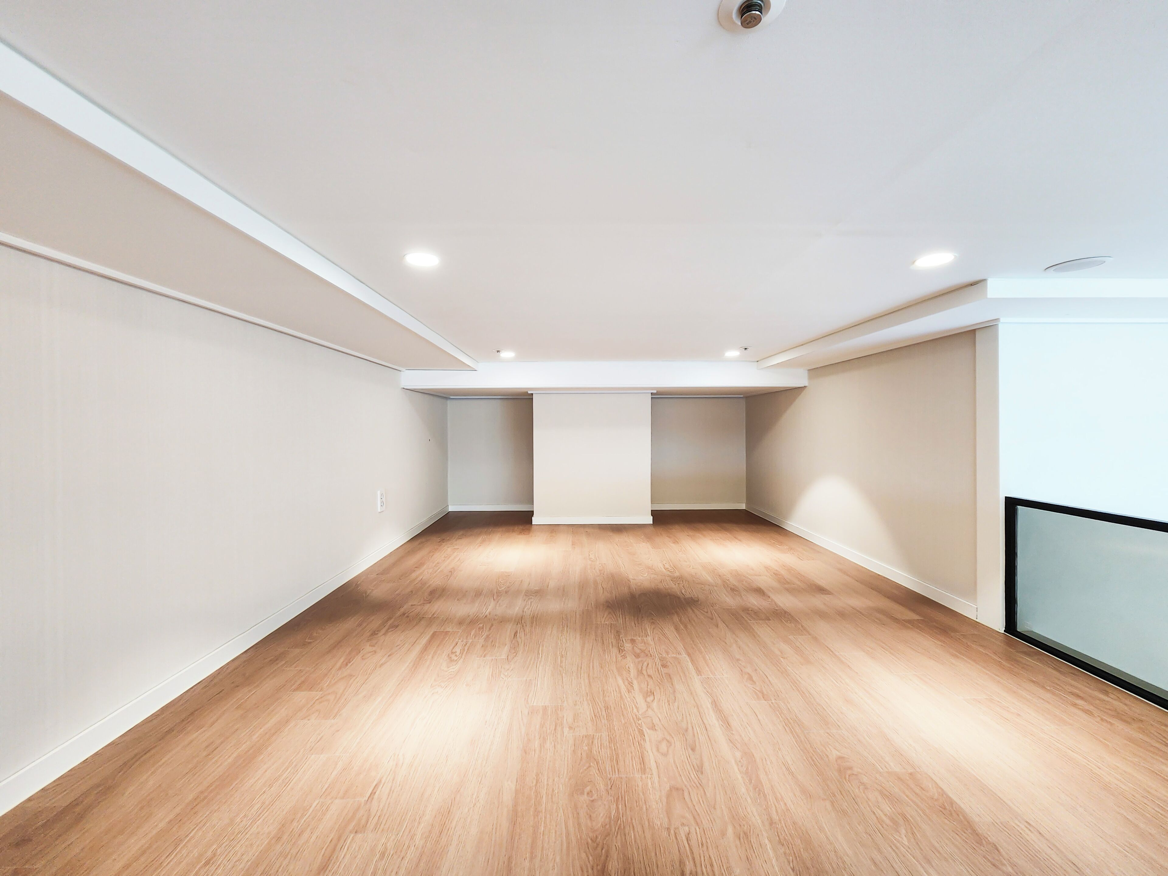 A spacious room with wooden flooring and white walls, featuring recessed ceiling lights and a visible closet.