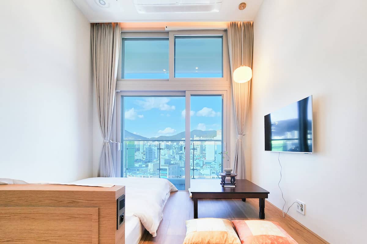 Una habitación de hotel con cama, una mesita, televisor y un ventanal con vistas a la ciudad.