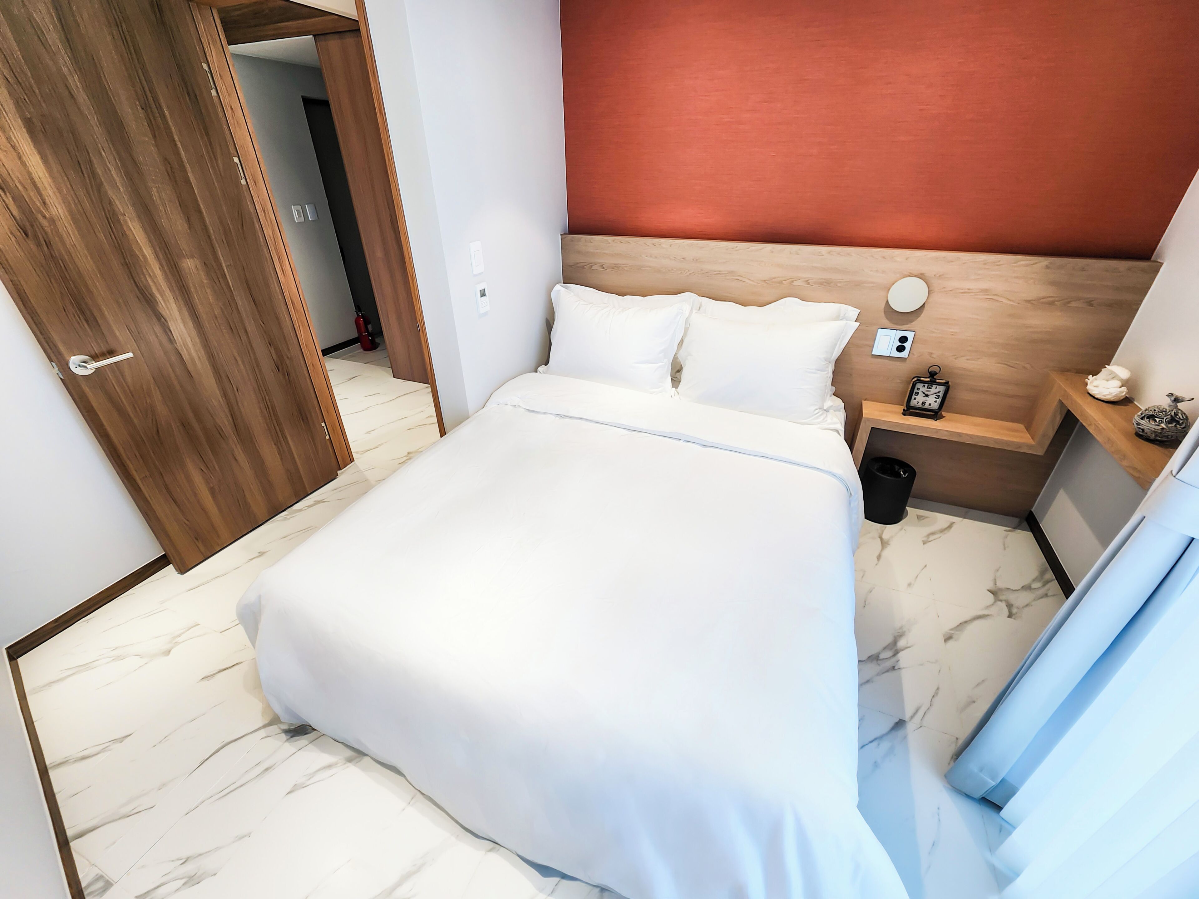 A hotel room with a bed, wooden headboard, bedside table, and a nightstand.