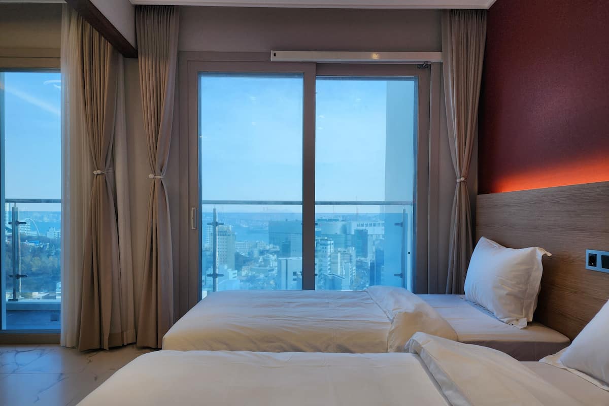 Habitación de hotel con dos camas, ventanas amplias y vista a la ciudad.