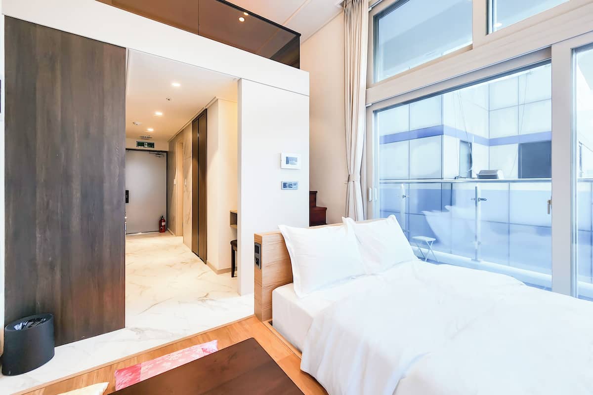 Una habitación de hotel moderna con una cama grande, un pequeño espacio de descanso y un balcón con vistas.
