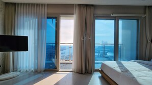 A modern hotel room with a large bed, a flat-screen TV, and a balcony with a city view. - Parami On (Busan)