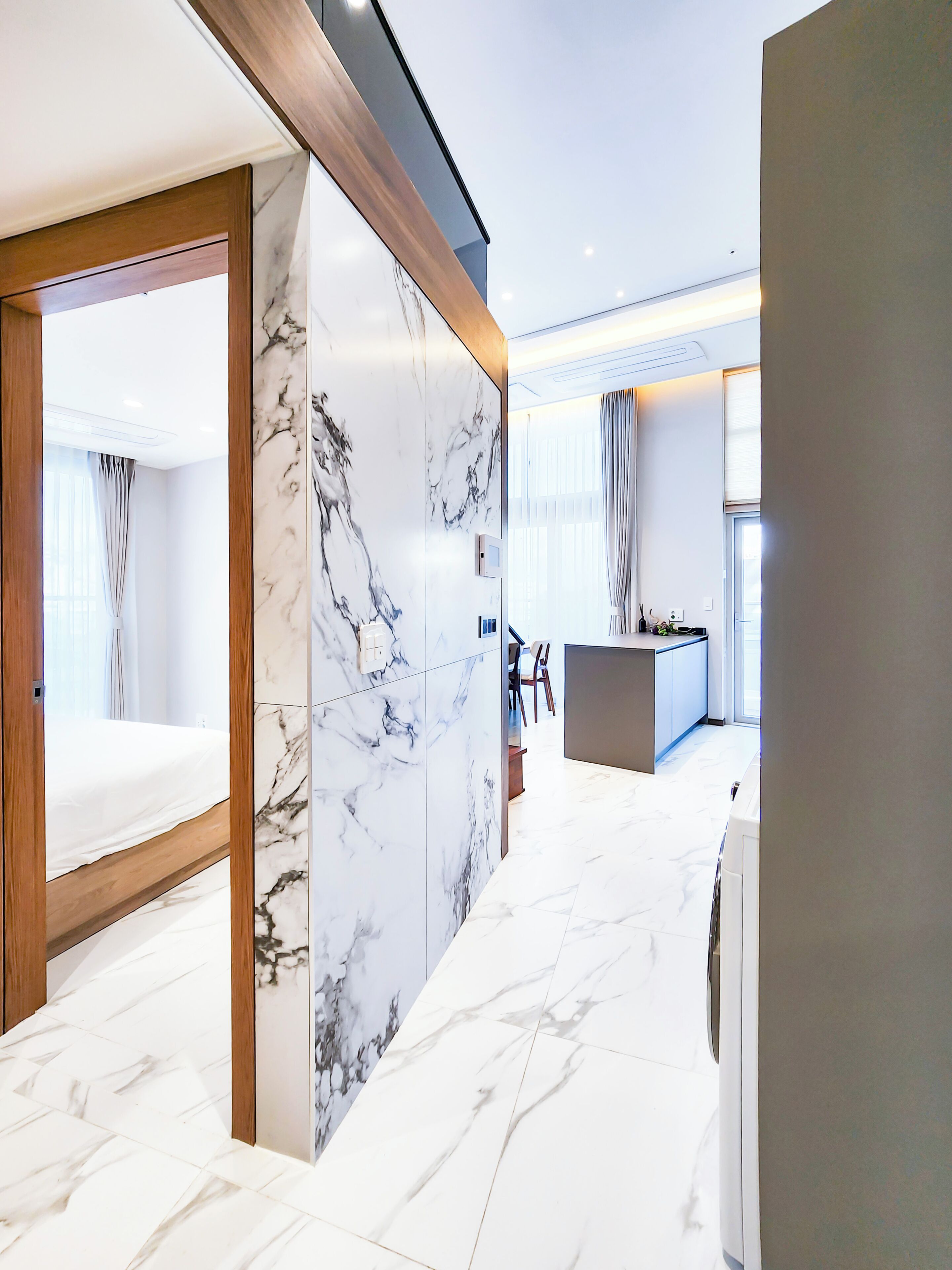 A modern hotel room with a marble wall, a wooden bed frame, and a view of the outside.