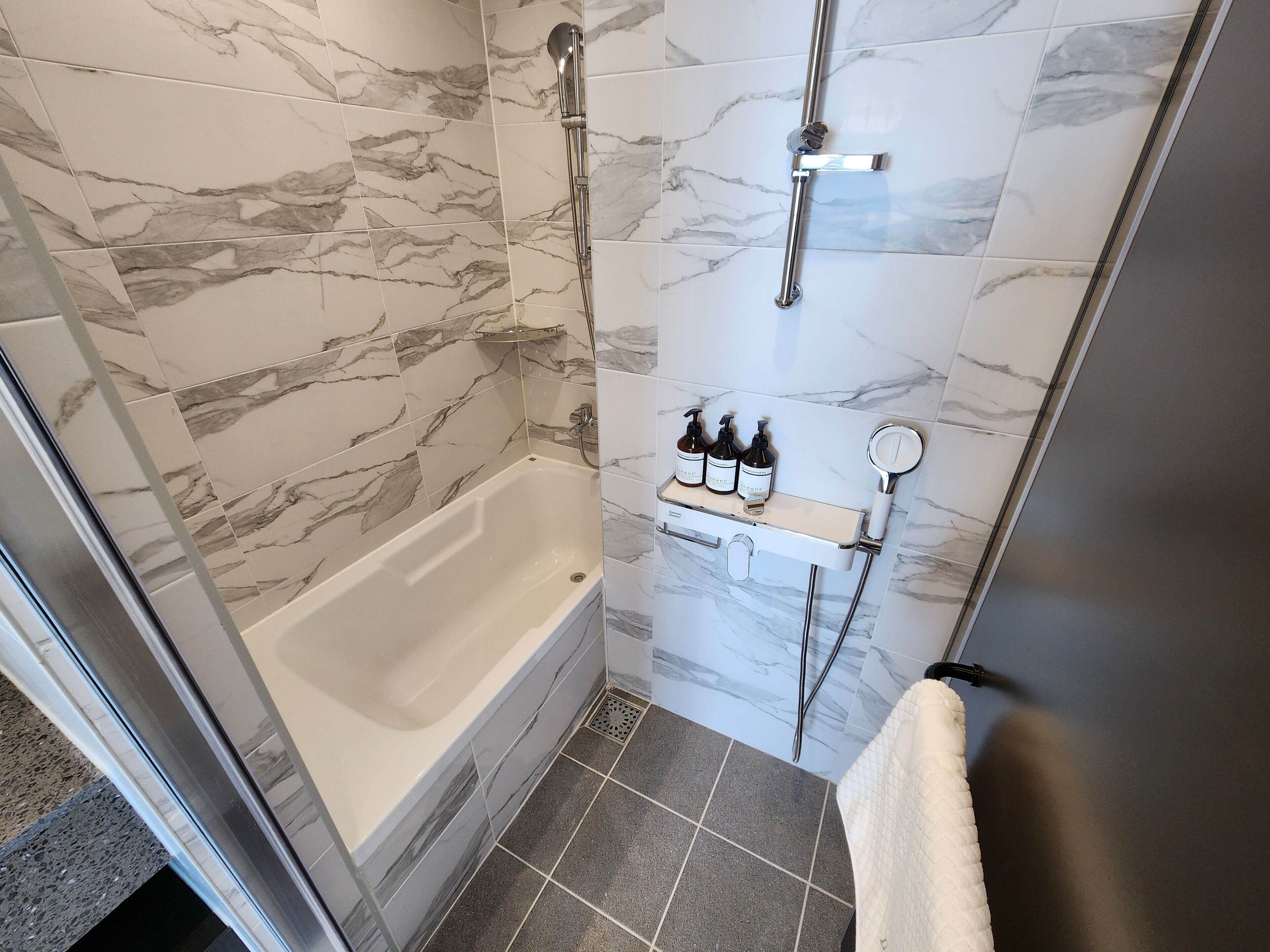 A bathroom with a bathtub, a shower, and a shelf with toiletries.