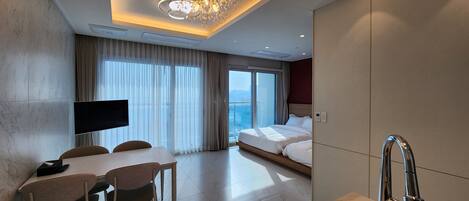 A modern hotel room with a large bed, a dining area with a table and chairs, a TV, and a bathroom with a sink and mirror.