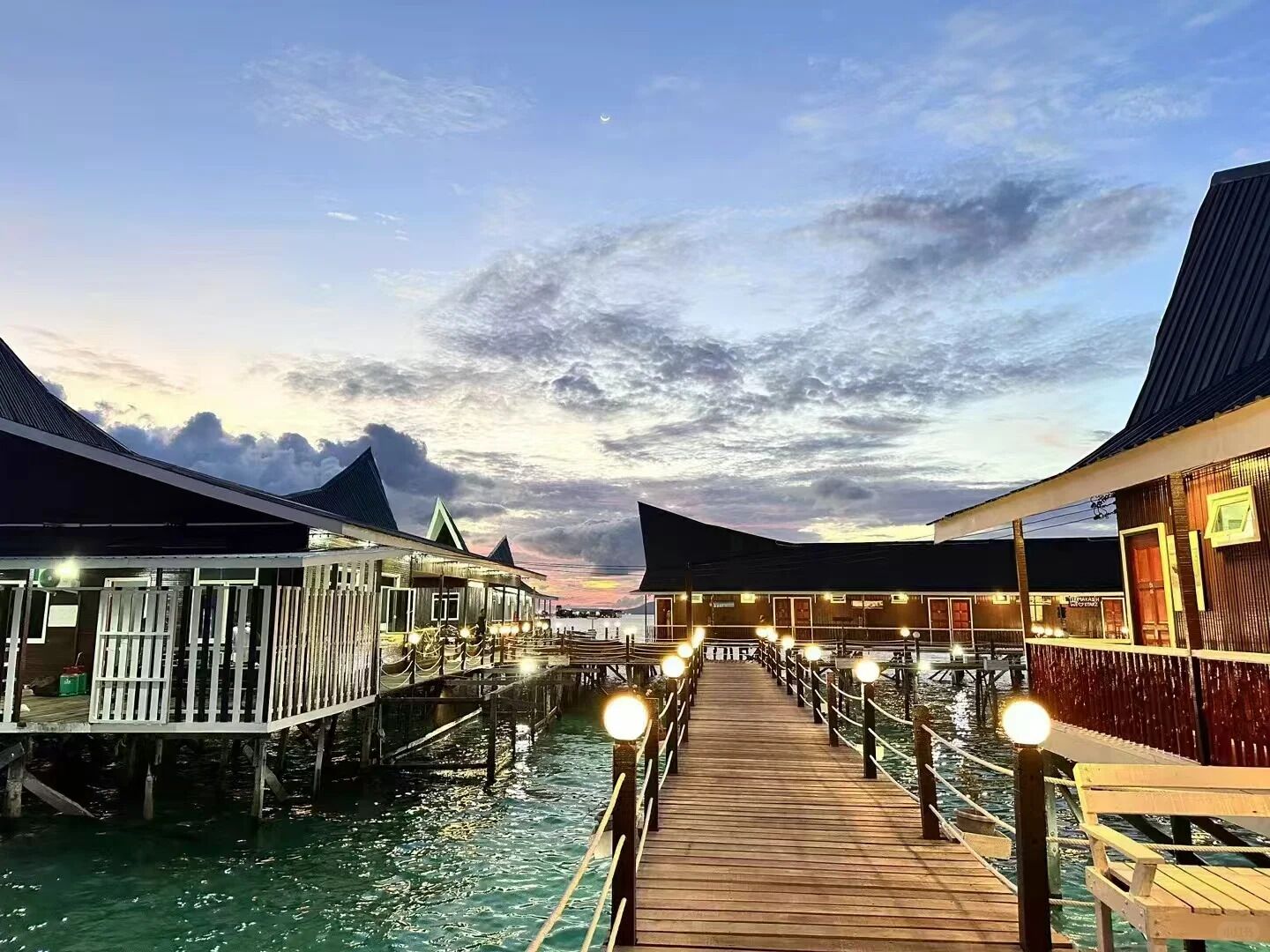 A wooden pier leading to overwater bungalows with a sunset sky.