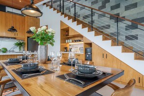 Uma cozinha moderna com armários de madeira, uma mesa de jantar posta para seis pessoas e uma escada com design de azulejos geométricos.