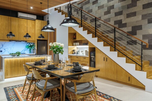 A modern kitchen with a wooden dining table, black pendant lights, and a staircase with a geometric wall design.