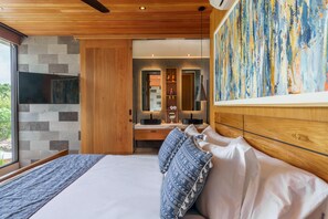 Quarto moderno com cama grande, cabeceira de madeira, TV integrada, parede de pedra e pintura abstrata colorida.