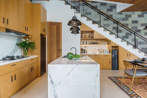 Uma cozinha moderna com armários de madeira, uma ilha de mármore e uma escada com design de azulejos geométricos.