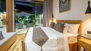Une chambre d’hôtel moderne dotée d’un grand lit, d’une tête de lit en bois, d’une porte en verre donnant sur un espace extérieur agrémenté de plantes et d’une table, ainsi que d’une grande œuvre d’art encadrée au mur.