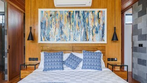 Une chambre avec un grand lit, une tête de lit en bois et un grand tableau abstrait au-dessus. Il y a deux tables de chevet avec des lampes.