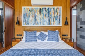A bedroom with a large bed, wooden headboard, and a large abstract painting above it. There are two bedside tables with lamps.