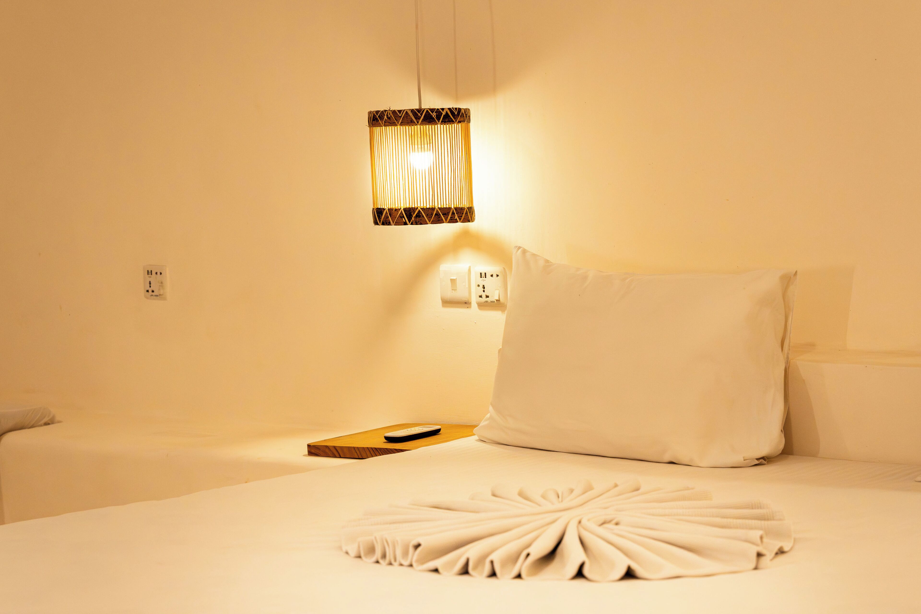 A hotel room with a neatly made bed, a remote control on the side, and a wall-mounted lamp.