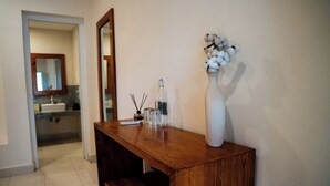 Une coiffeuse en bois avec un miroir, un vase contenant des plantes de coton et une bouteille.