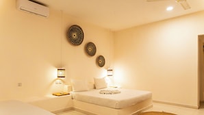 Une chambre d’hôtel comprenant un lit, des tables de chevet, un climatiseur fixé au mur et des œuvres d’art décoratives accrochées au mur.
