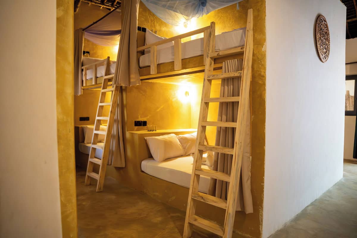 Habitación con literas de madera, una mesita de noche y una lámpara fijada a la pared.