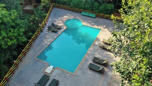 A rectangular swimming pool surrounded by a yellow and red fence, with lounge chairs and a bench around the perimeter. - Tiger King Resort (Chimur)