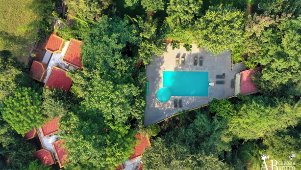 An aerial view of a property with a swimming pool, surrounded by dense greenery and several red-roofed buildings. - Tiger King Resort (Chimur)
