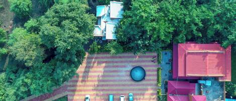 An aerial view of a property with a parking area, a swimming pool, and a red-roofed building.