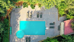 Vue aérienne d’un espace piscine comprenant une piscine rectangulaire, entourée d’une terrasse dallée et délimitée par un petit muret.