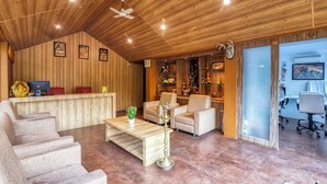 A spacious room with a wooden ceiling, a reception desk, comfortable seating, and a large window. - Tiger King Resort (Chimur)