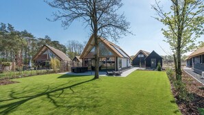 A modern house with a large glass front, a well-maintained lawn, and a tree in the center. - Thatched bungalow with private terrace (Baarle-nassau)