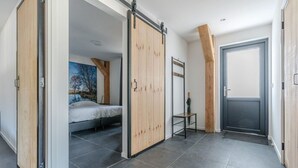 A modern bedroom with a bed, a sliding wooden wardrobe, a small table, and a grey door. - Thatched bungalow with private terrace (Baarle-nassau)