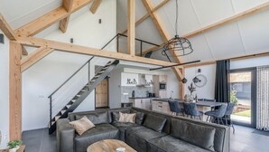 A modern living space with a sectional sofa, a dining table, and a kitchen in the background. - Thatched bungalow with private terrace (Baarle-nassau)