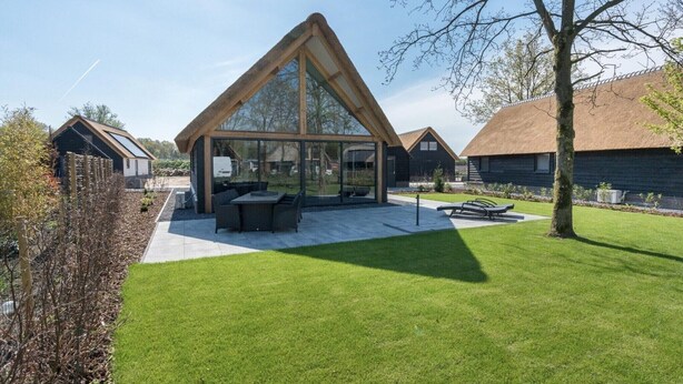 A modern house with a large glass conservatory, a patio with outdoor furniture, and a well-maintained lawn. - Thatched bungalow with private terrace (Baarle-nassau)