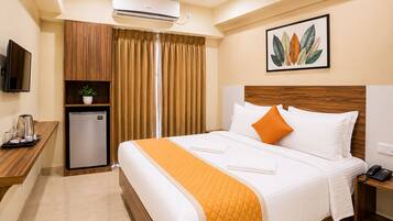 Una habitación de hotel con una cama, un escritorio con cafetera, un mini refrigerador, aire acondicionado y un televisor montado en la pared.