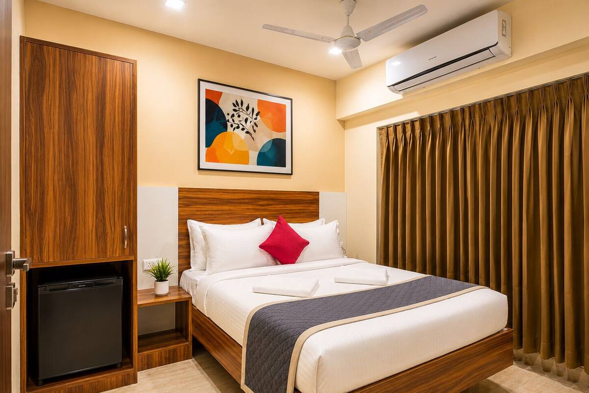 A hotel room with a bed, a ceiling fan, an air conditioner, a small table with a plant, and a wardrobe.