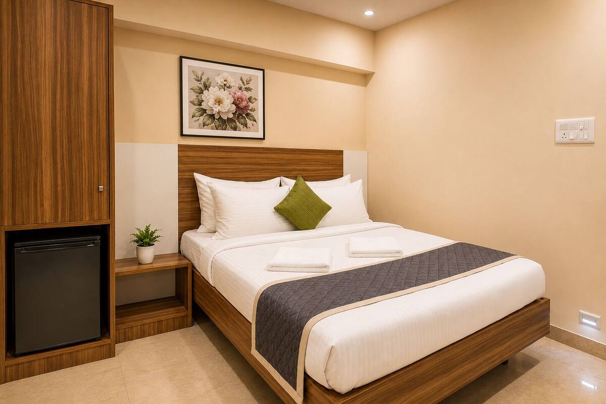 A hotel room with a bed, a small bedside table with a plant, a wall-mounted light, and a wooden wardrobe.