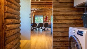 Interior de una cabaña de troncos con comedor, lavadora y paredes de madera.
