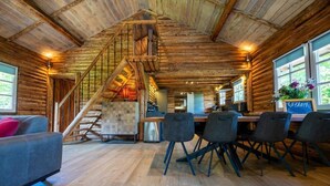 Interior rústico de una cabaña de troncos, con comedor, escalera y cocina.