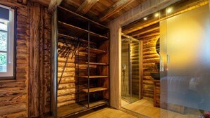 Interior de una cabaña de troncos con ducha envuelta en cristal, estantes de madera y un cuadro en la pared.