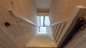 A wooden interior with a staircase, white railings, and a window at the top. - Seaside Holiday Home with Garden (Groote Keeten)