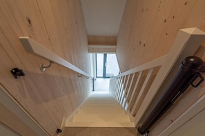 A wooden interior with a staircase, white railings, and a window at the top.