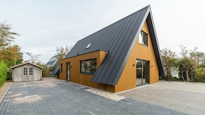 A modern house with a sloped roof, a small attached garage, and a paved driveway. - Seaside Holiday Home with Garden (Groote Keeten)